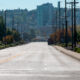 Wide empty street in a city neighborhood, power poles line both sides with trees and distant buildings on the skyline.