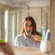 Woman brushing her teeth at bathroom sink, seen in the mirror, with a blue toothbrush.