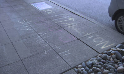 Sidewalk chalk messages in white and purple along a curb, with a parked car wheel visible.