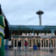 Person in a green jersey with 'PAYTON' and the number 20 stands at the left, facing Alaska Airlines Atrium entrance with the Space Needle in the distance on a cloudy day.