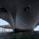 Low-angle view of a colossal ship hull towering above the water with several paddleboarders in the foreground.