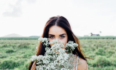 Woman in a field holding white baby's breath flowers in front of her face, revealing her blue eyes.