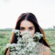 Woman in a field holding white baby's breath flowers in front of her face, revealing her blue eyes.