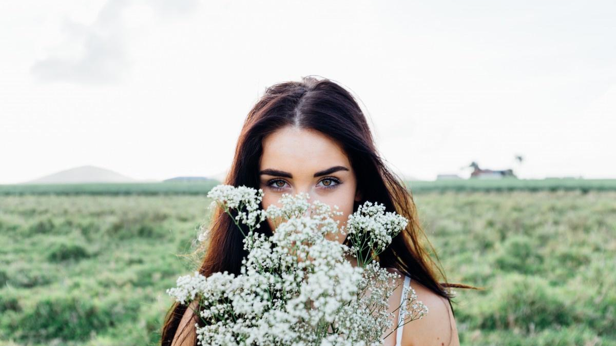 Woman in a field holding white baby's breath flowers in front of her face, revealing her blue eyes.