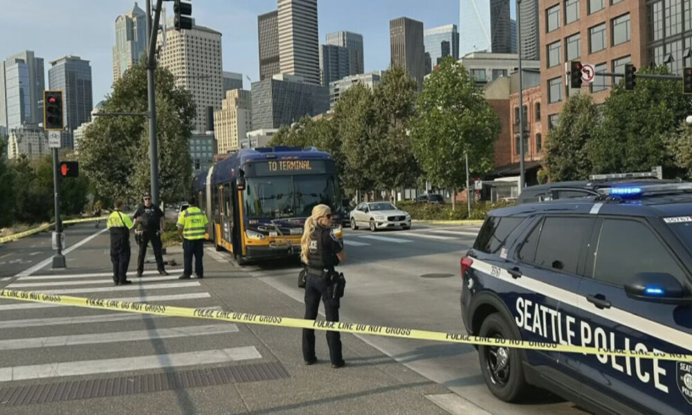 Seattle street scene with police tape and officers guarding a bus near downtown skyline.
