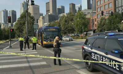 Seattle street scene with police tape and officers guarding a bus near downtown skyline.