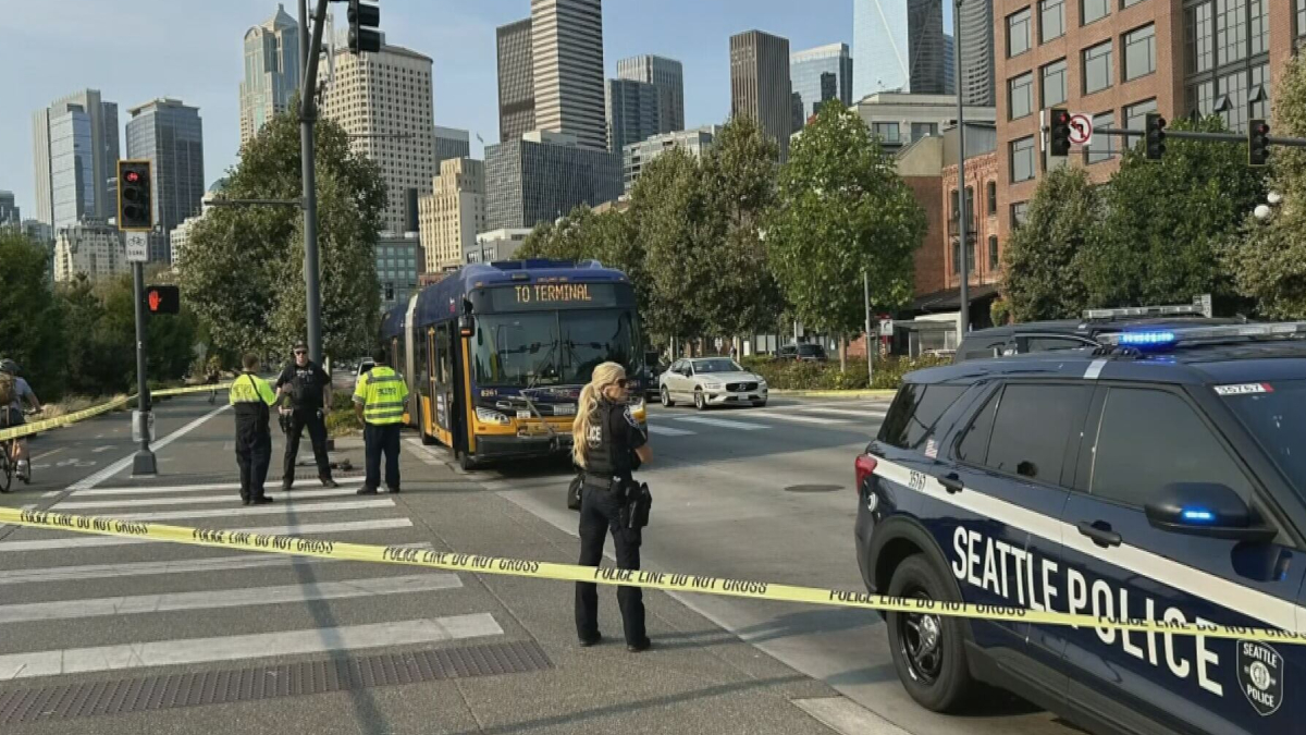 Seattle street scene with police tape and officers guarding a bus near downtown skyline.