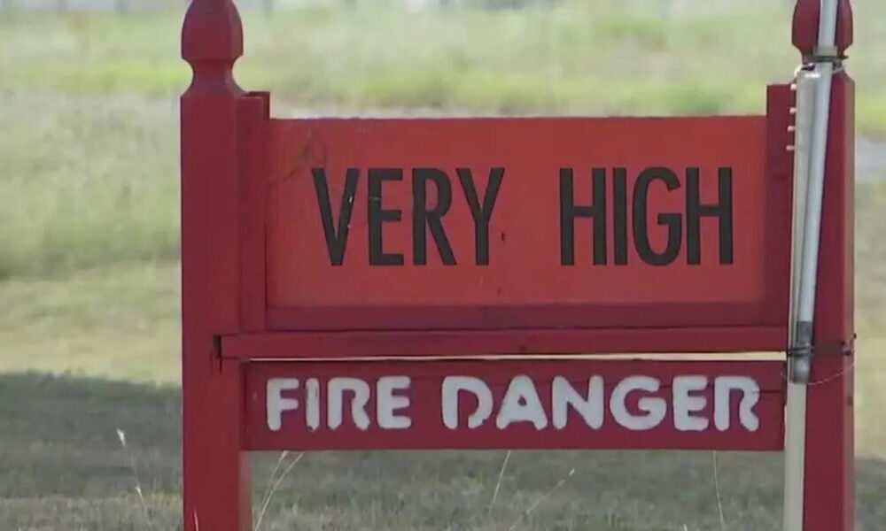 Red warning sign reading 'VERY HIGH' above 'FIRE DANGER' in a grassy outdoor area.