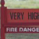 Red warning sign reading 'VERY HIGH' above 'FIRE DANGER' in a grassy outdoor area.