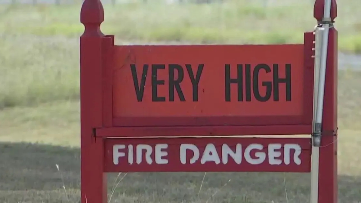 Red warning sign reading 'VERY HIGH' above 'FIRE DANGER' in a grassy outdoor area.