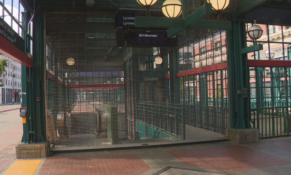 Closed metal security gates block the entrance to a subway station, with overhead signs reading 'ID/Chinatown' and hanging lantern-style lights above.