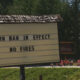 Outdoor roadside sign reading 'BURN BAN IN EFFECT' and 'NO FIRES' with trees in the background nearby construction cones.