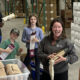 Smiling volunteers in a warehouse packaging supplies for donation or charity drive, with boxes and gear in the background.