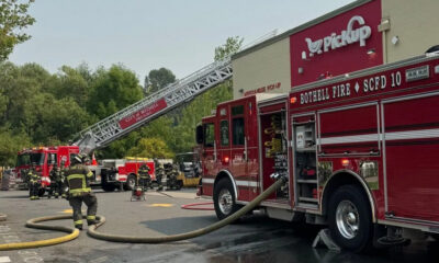 Firefighters battle a blaze near a red storefront; a tall ladder extends from a fire truck toward the building.