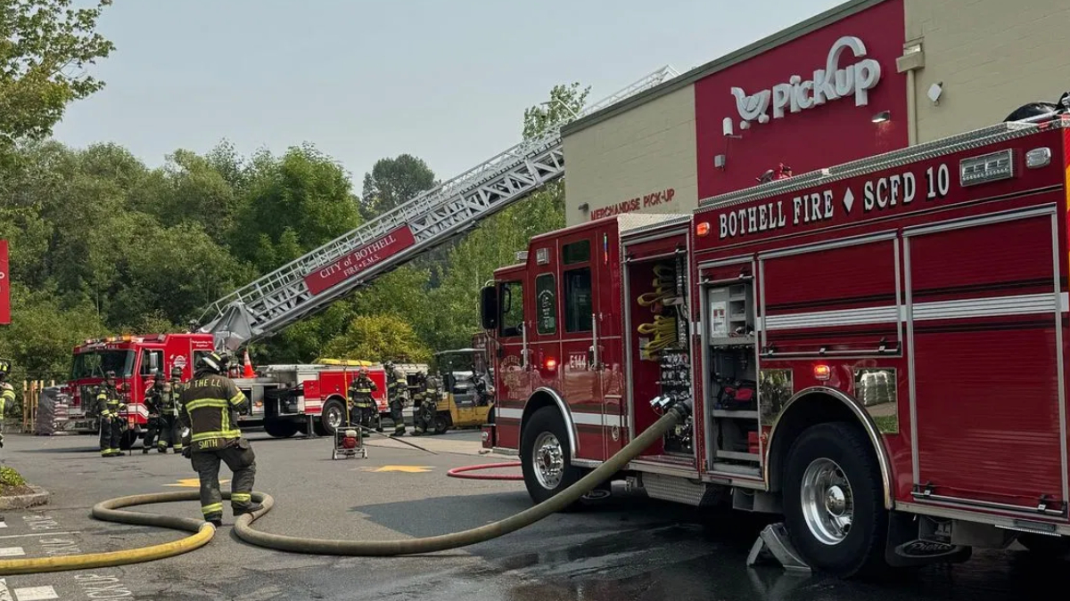 Firefighters battle a blaze near a red storefront; a tall ladder extends from a fire truck toward the building.