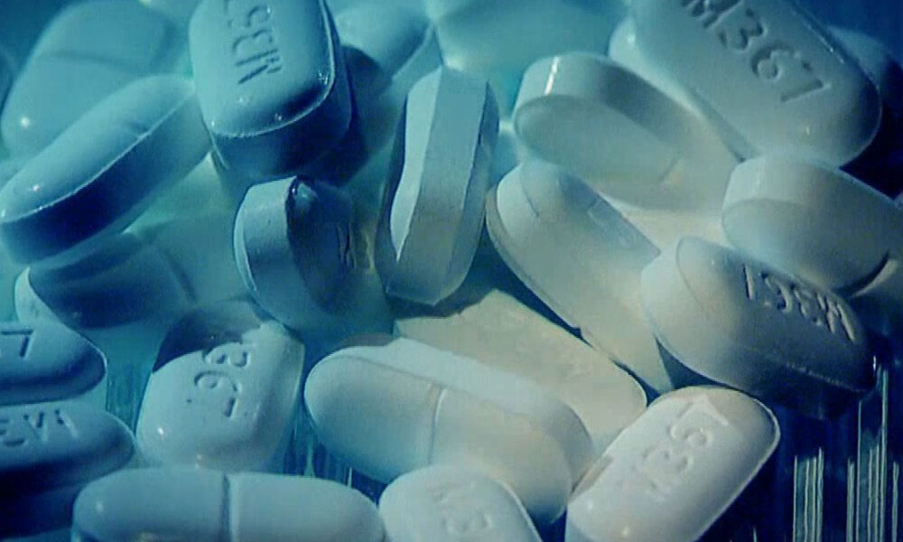 White oblong pills with imprints scattered in a blue-tinted close-up scene.
