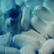 White oblong pills with imprints scattered in a blue-tinted close-up scene.
