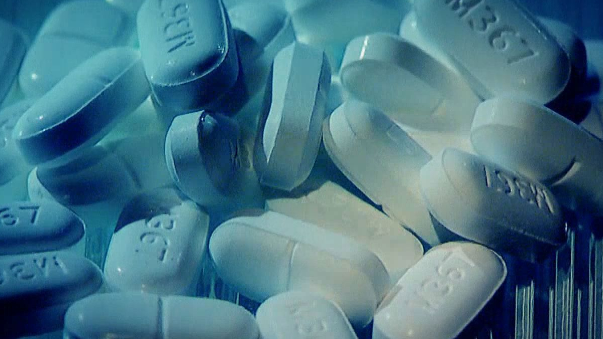 White oblong pills with imprints scattered in a blue-tinted close-up scene.