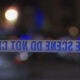 Police tape reading 'CRIME SCENE DO NOT CROSS' across a dimly lit street with blurred city lights in the background.