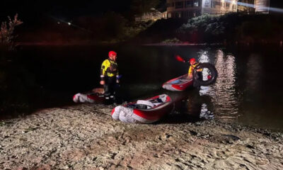 Nighttime riverbank rescue with inflatable boats and two responders in yellow suits and red helmets.
