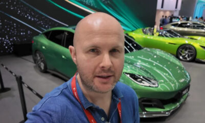 Man taking a selfie at a car show, with a bright green sports car in the foreground and other cars in the background.