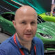 Man taking a selfie at a car show, with a bright green sports car in the foreground and other cars in the background.