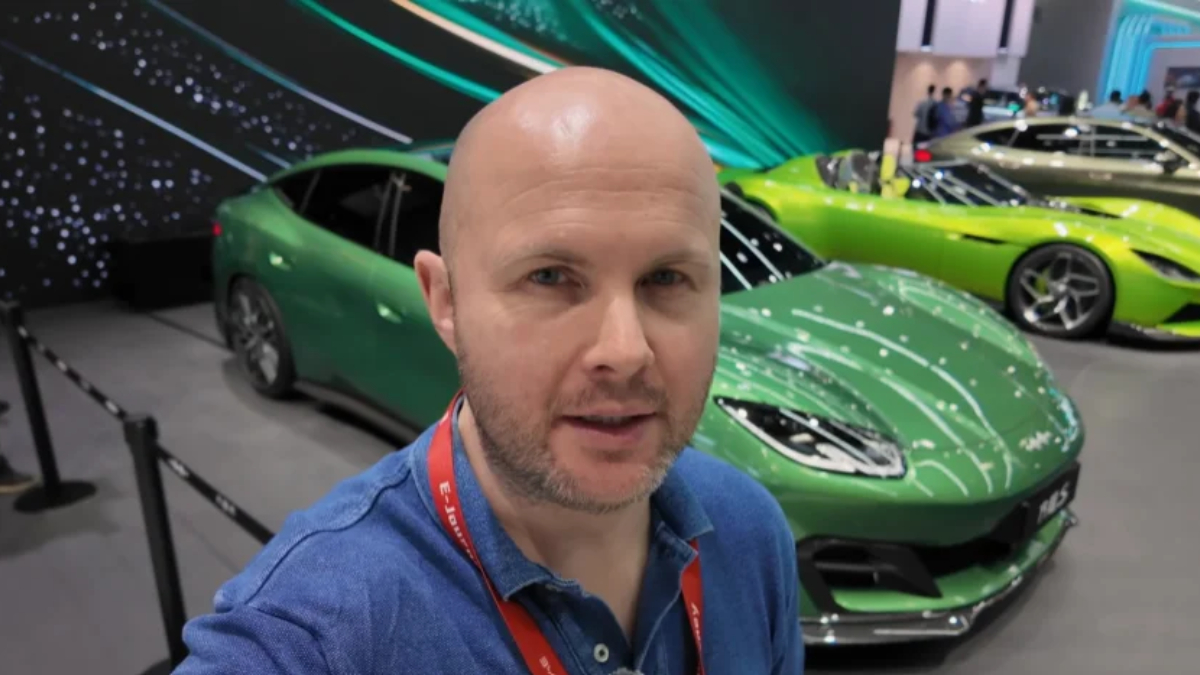 Man taking a selfie at a car show, with a bright green sports car in the foreground and other cars in the background.