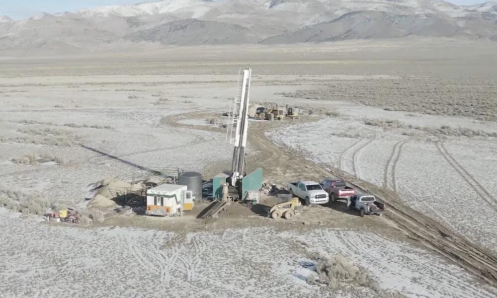 Oil drilling rig setup in a snowy desert with support trailers and multiple pickup trucks nearby. A remote field site under mountains in winter.
