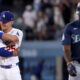 Two Los Angeles Dodgers players hug in celebration on the field as a Seattle Mariners player walks away in the foreground.