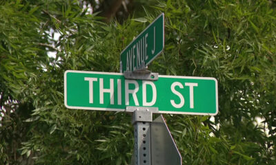 Green street sign reading 'THIRD ST' with a smaller 'AVENUE J' sign above, against leafy background.