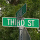 Green street sign reading 'THIRD ST' with a smaller 'AVENUE J' sign above, against leafy background.
