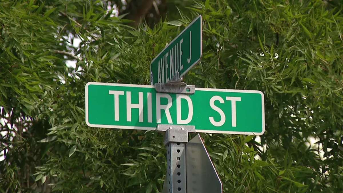 Green street sign reading 'THIRD ST' with a smaller 'AVENUE J' sign above, against leafy background.