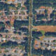 Aerial view of a residential neighborhood with tree-lined streets and rows of single-family houses around a central vertical road.