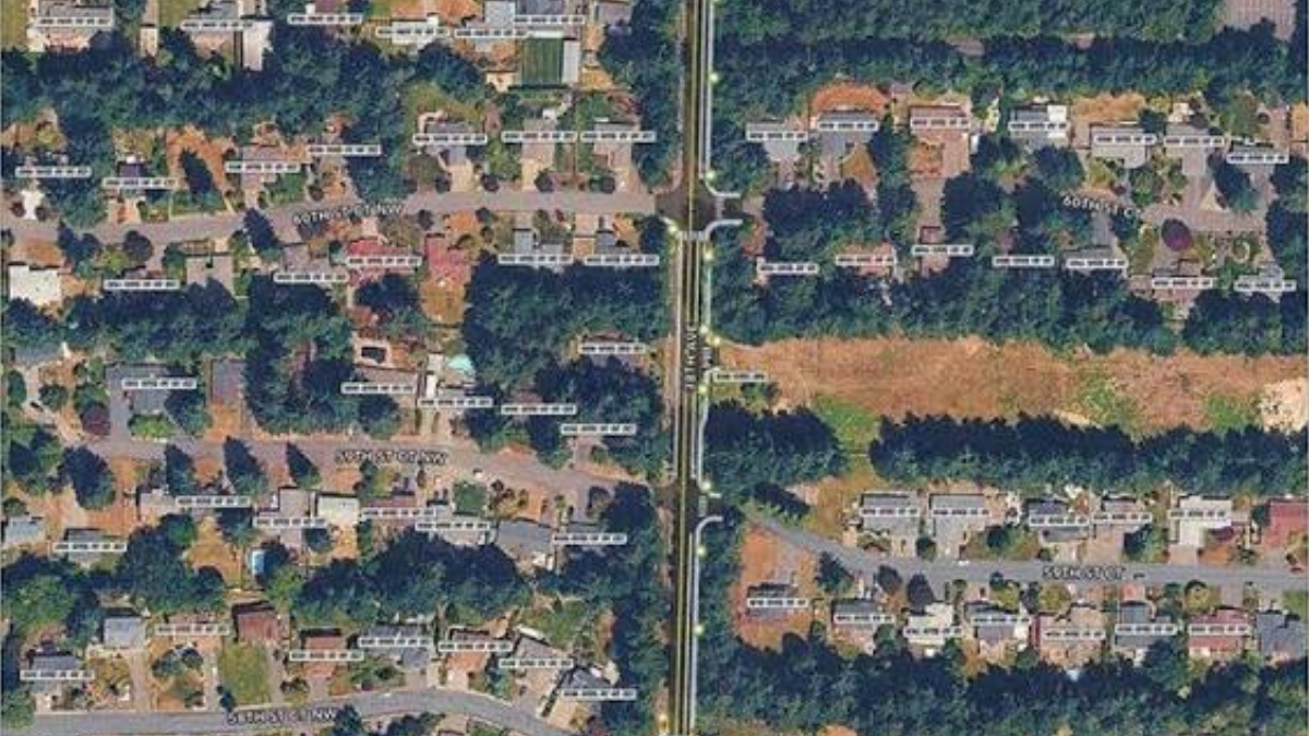 Aerial view of a residential neighborhood with tree-lined streets and rows of single-family houses around a central vertical road.