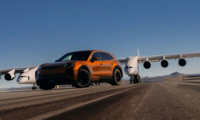 Orange SUV on an airport runway with a large white jet in the background under a clear blue sky.