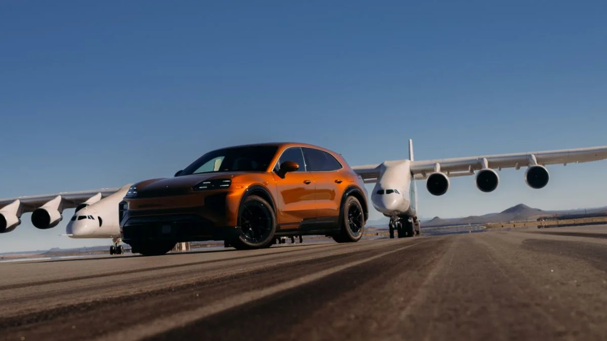 Orange SUV on an airport runway with a large white jet in the background under a clear blue sky.