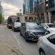 Bus and several cars stuck in traffic on a city street with tall modern buildings in the background and a yellow car on the left edge.