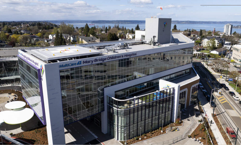 Aerial view of MultiCare Mary Bridge Children’s Hospital with glass exterior and surrounding cityscape by a body of water in the distance.