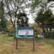 Chain-link fence surrounds a small park area with a sign about the North Slope Historic Park project in the foreground.