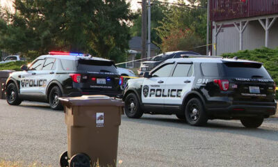 Two Tacoma Police Department SUVs with red and blue lights flashing, parked on a residential street with a trash bin in the foreground.