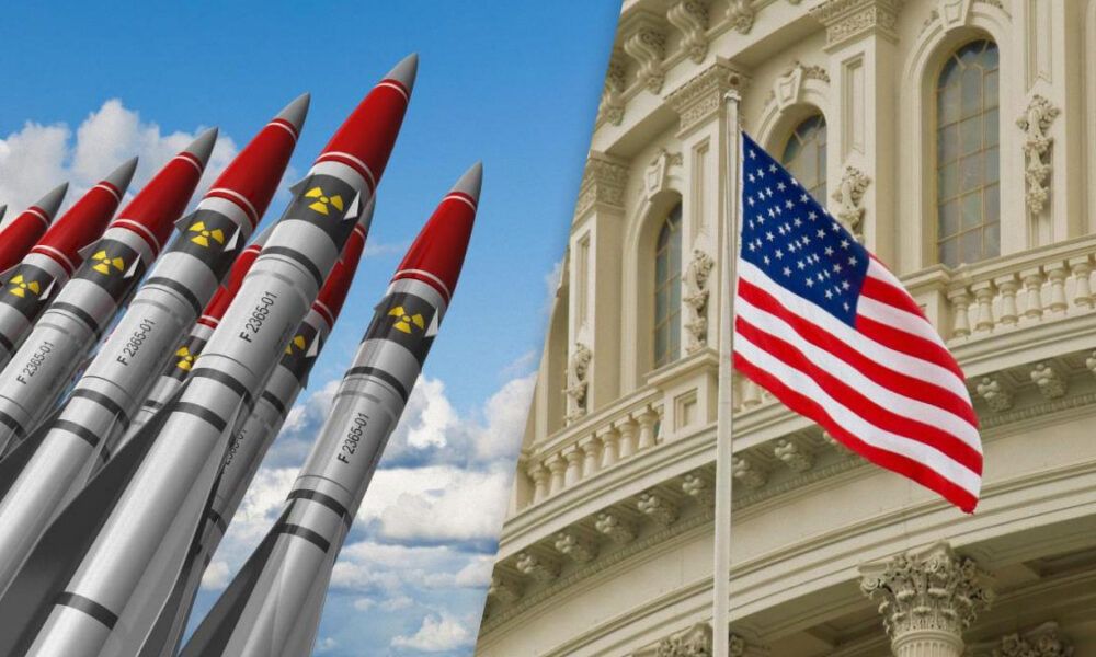 Row of missiles pointed upward beside a waving U.S. flag in front of a grand government building.