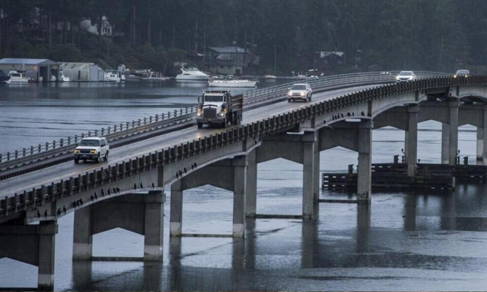 Bridge carrying traffic over a calm harbor, with a truck and several cars crossing and boats in the background.