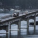 Bridge carrying traffic over a calm harbor, with a truck and several cars crossing and boats in the background.