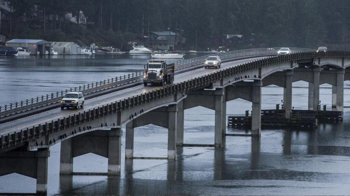 Bridge carrying traffic over a calm harbor, with a truck and several cars crossing and boats in the background.