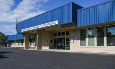Blue-roofed educational services center building with glass doors and flagpole in front; parking lot visible outside the entrance.