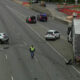 Highway crash scene with a silver SUV burned-out on the left, a white SUV in the middle, and a large box truck pulled over on the right as responders work nearby.