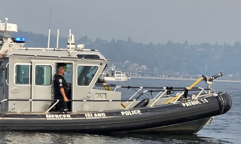 Police patrol boat on calm water with officer standing at the cabin door, blue emergency lights visible on top.