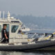 Police patrol boat on calm water with officer standing at the cabin door, blue emergency lights visible on top.