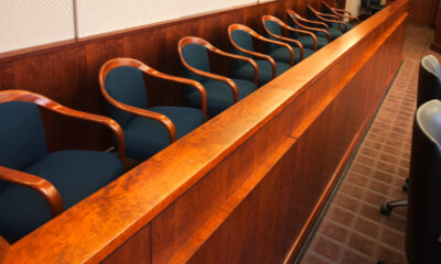 Row of blue upholstered chairs with wooden arms along a glossy wooden barrier in a formal meeting or courtroom setting