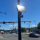 Solar panel mounted on a streetlight at a busy intersection with cars and clear blue sky behind it.